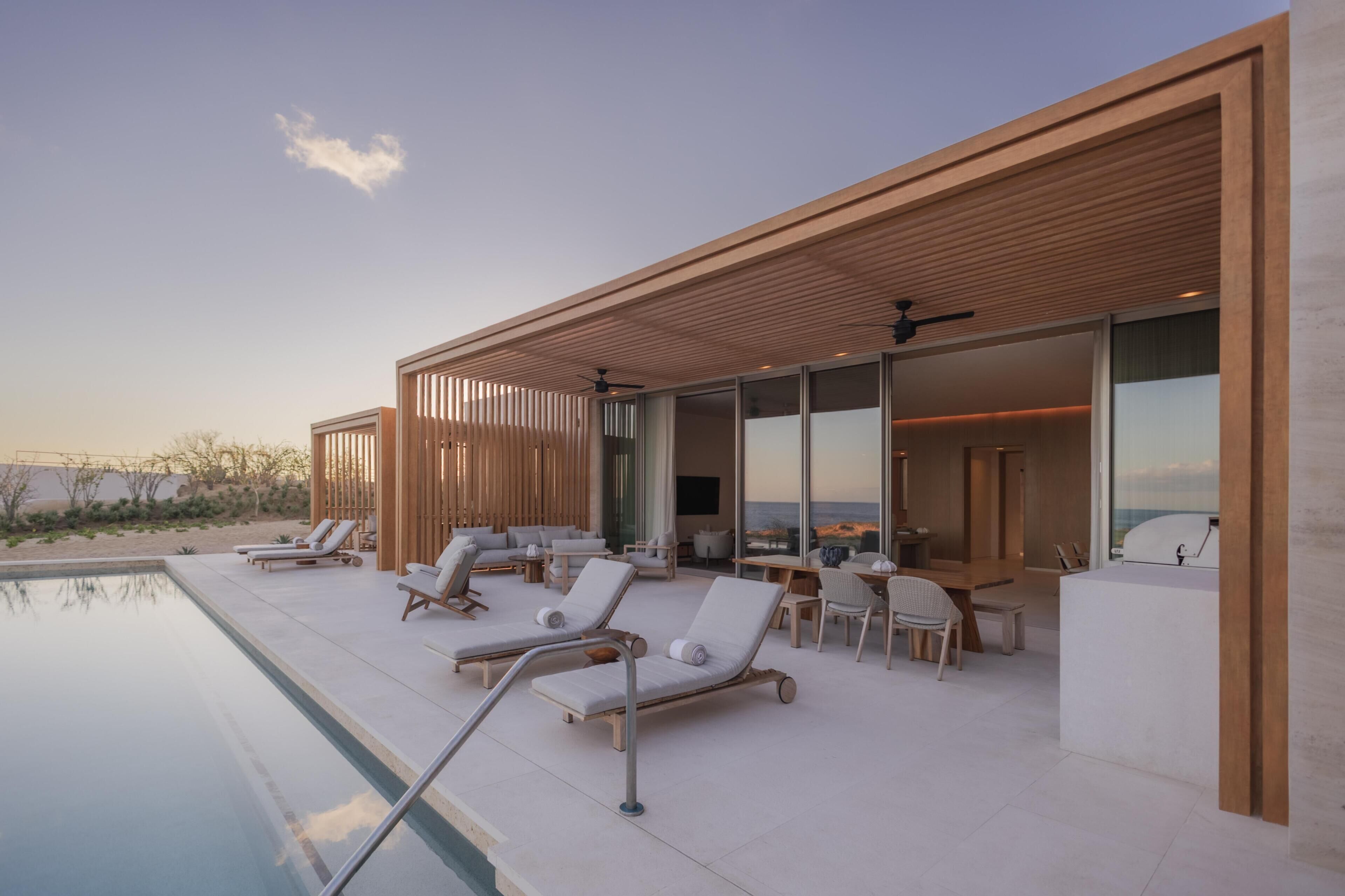 Un espace piscine extérieur moderne, doté de chaises longues et d’un coin repas, avec vue sur une étendue d’eau.
