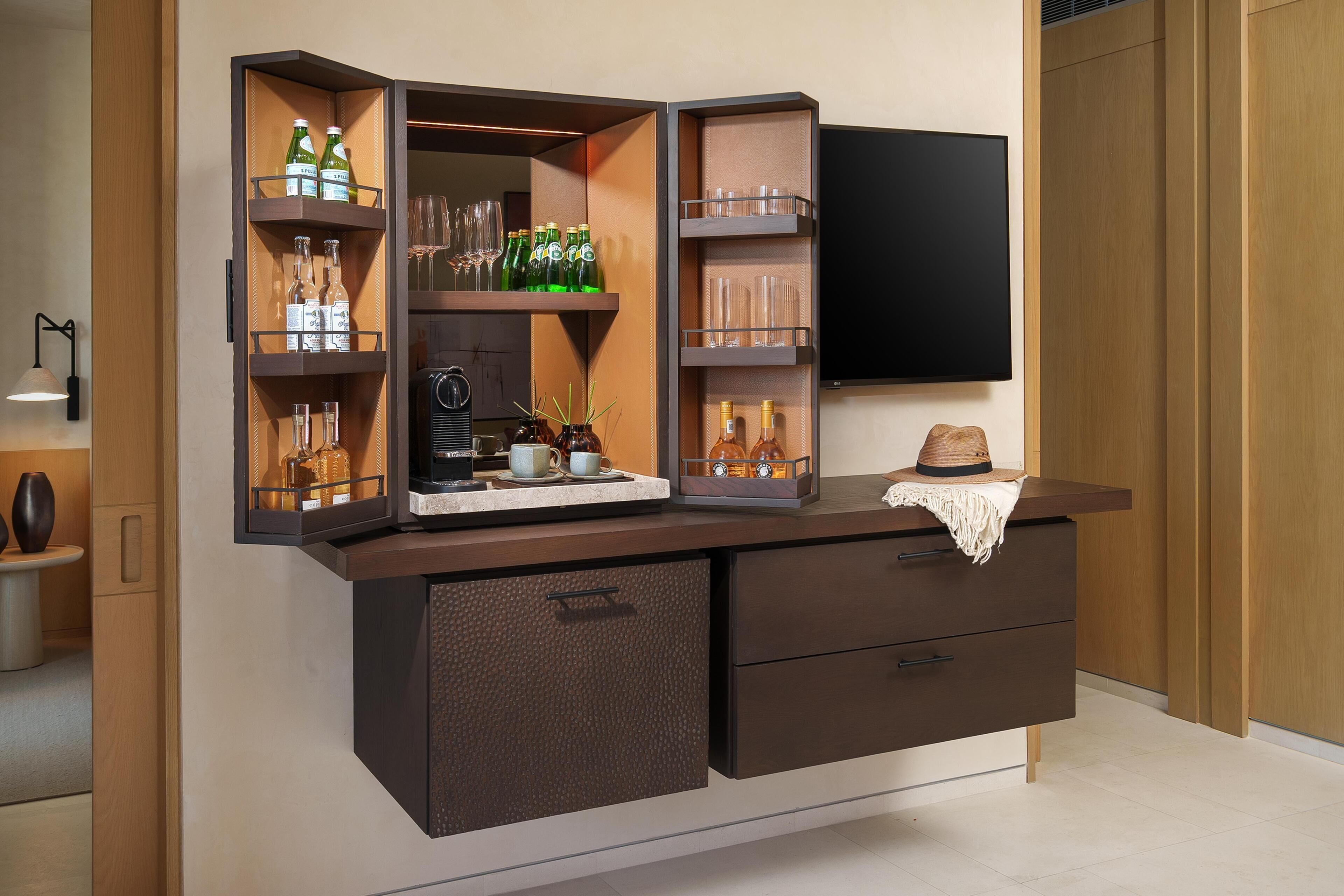 A bar area with shelves holding bottles and glasses, a television mounted on the wall, and a small table with a hat.