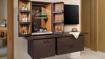 A bar area with shelves holding bottles and glasses, a television mounted on the wall, and a small table with a hat.