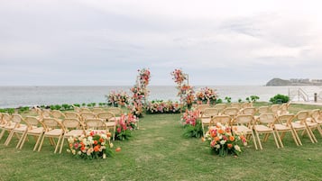 An outdoor wedding setup with chairs arranged in rows facing a floral archway.