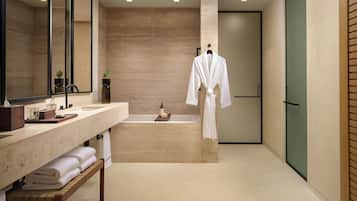 A modern bathroom with a large mirror, a bathtub, and a robe hanging on a rack.