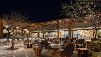 An outdoor seating area with tables and chairs, a bar, and a covered section with large windows.