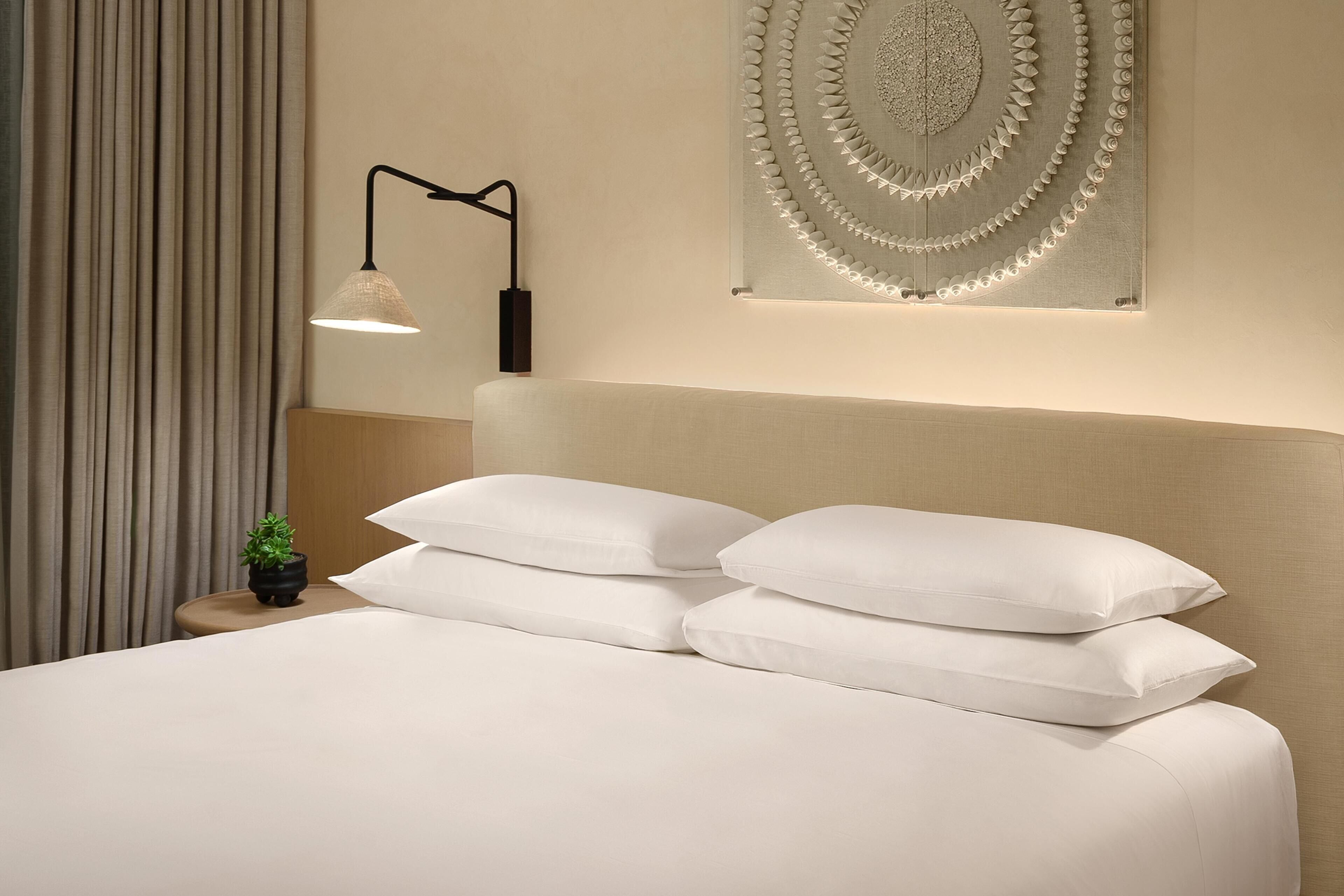 A neatly made bed with white bedding, a wall-mounted lamp, and a decorative wall piece.
