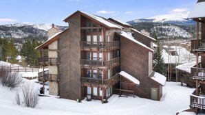 Una cabaña de madera de varios pisos con balcones, con una imponente montaña nevada al fondo.