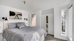Un dormitorio con una cama, dos lámparas de pared, un cuadro y vistas a través de una ventana.
