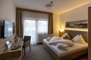 A hotel room with a bed, a desk, a chair, a TV, a painting on the wall, and a window with curtains. - Hotel Turracherhof (Stadl-Predlitz)