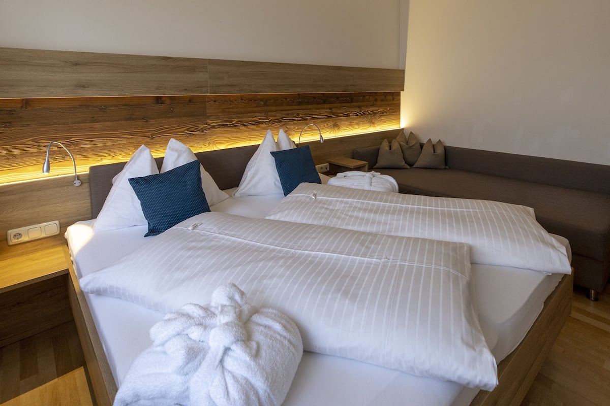 A hotel room with two beds, a wooden headboard, a nightstand, and a sofa.