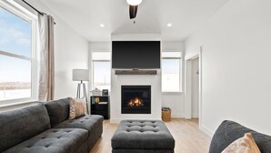 Una sala moderna con chimenea, sofás grises y un televisor de pantalla plana.