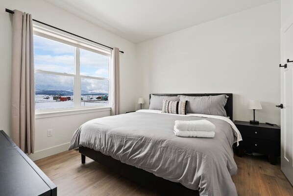 A bedroom with a large window, a bed, a bedside table, and a view of a snowy landscape.