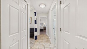 A hallway with white doors, a bed, a nightstand, and a lamp. - Ocean Paradise 1425-Ocean Views-Sleeps 7 (Panama City Beach)