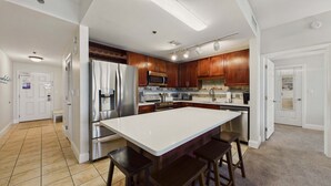 A kitchen with a central island, stainless steel appliances, wooden cabinets, and a tiled floor. - Ocean Paradise 1425-Ocean Views-Sleeps 7 (Panama City Beach)