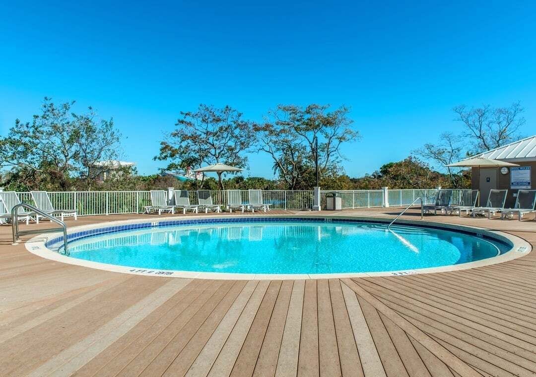 A pool area with a wooden deck, lounge chairs, and a fenced swimming pool.