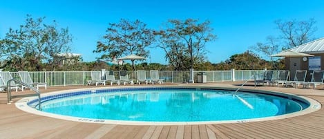 Un área de piscina con muelle de madera, sillas de descanso y piscina cercada.