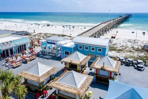 A beachside resort with a pier, thatched-roof huts, and a beachfront bar. - Ocean Paradise 1425-Ocean Views-Sleeps 7 (Panama City Beach)