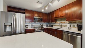 Una cocina con electrodomésticos de acero inoxidable, armarios de madera y encimera blanca.