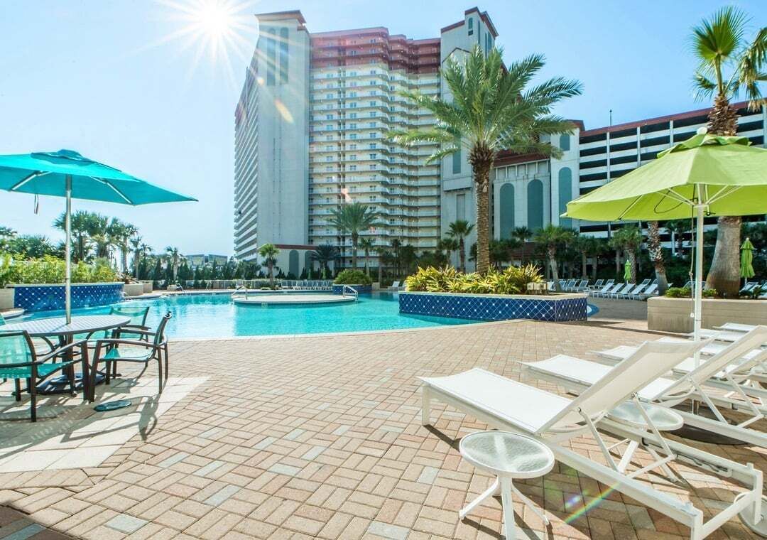 A hotel pool area with lounge chairs, umbrellas, and a large building in the background.