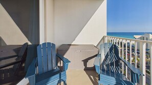A balcony with two blue Adirondack chairs, a small table, and a view of the ocean. - Ocean Paradise 1425-Ocean Views-Sleeps 7 (Panama City Beach)