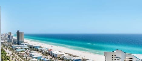 A coastal cityscape with a beach, buildings, and a clear sky.