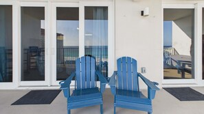 Two blue Adirondack chairs outside a building with a glass door and a white wall.