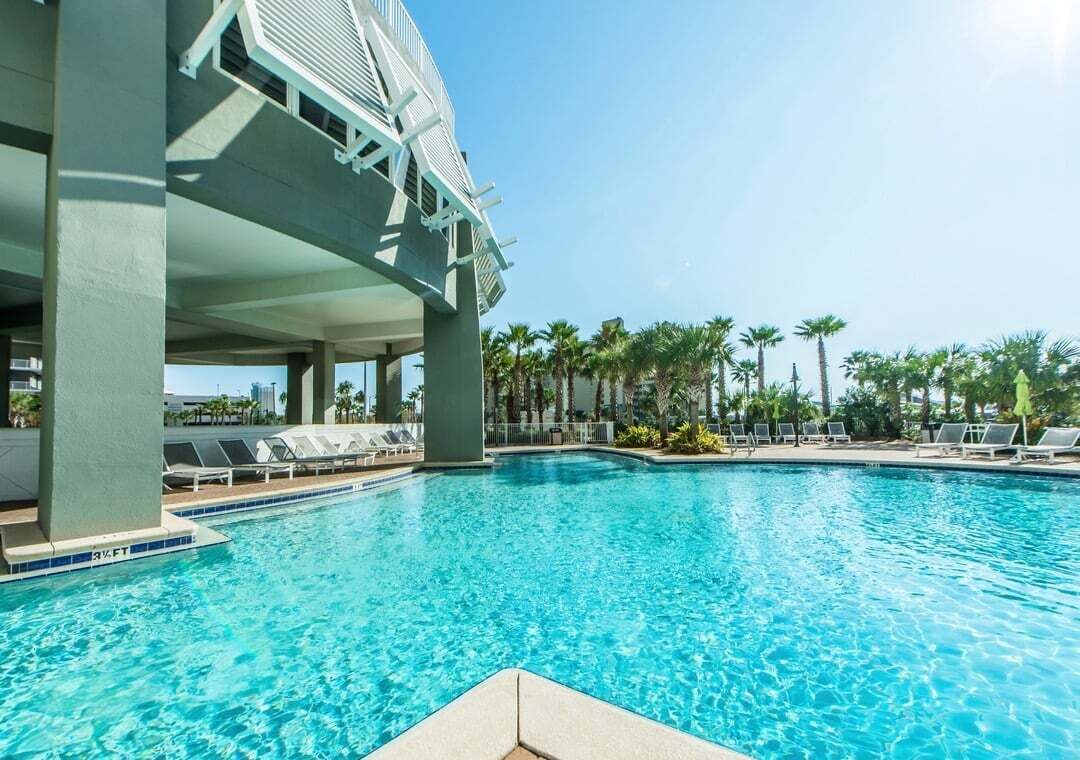 Una piscina con sillones de descanso y palmeras al fondo.