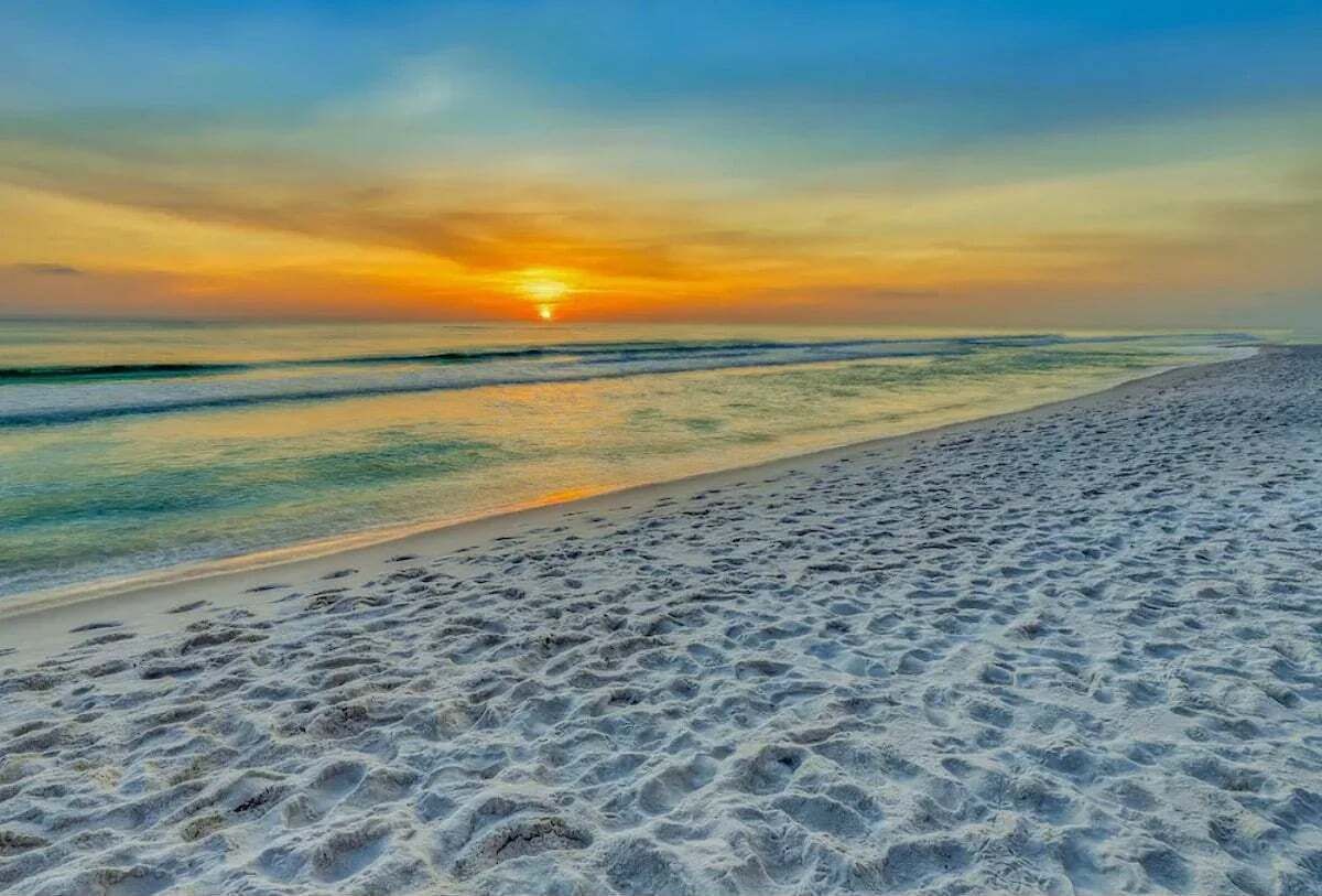 Uma praia com pôr do sol, areal e mar calmo.