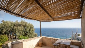 A terrace with a view of the sea, featuring a table and chairs, and a thatched roof. - AMORE RENTALS - Villa Margherita with Sea View and Swimming Pool (Amalfi)