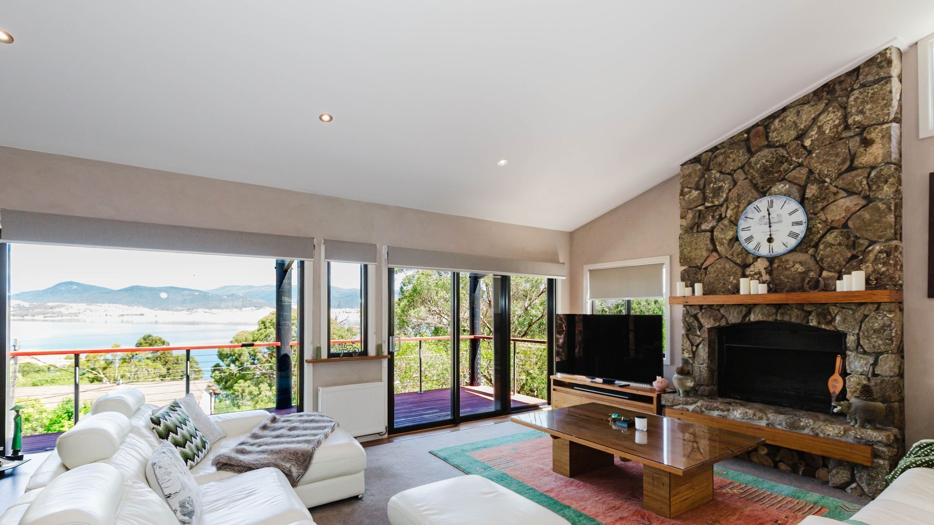 A modern living room with a stone fireplace, a large flat-screen TV, and a sofa.