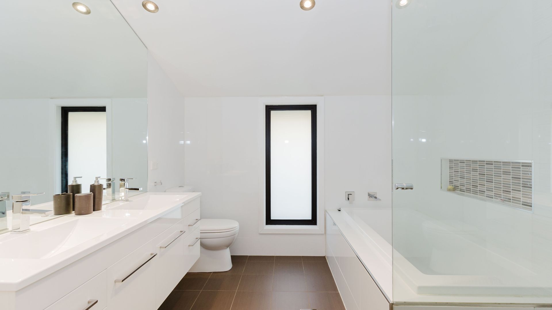 A modern bathroom with a white vanity, a toilet, and a glass-enclosed shower area.