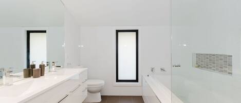 A modern bathroom with a white vanity, a toilet, and a glass-enclosed shower area.