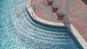 Ein rechteckiger Pool mit geschwungener Kante, umgeben von einem Ziegelweg und weißen Säulen.