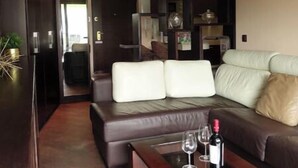 Ein modernes Wohnzimmer mit einem dunkelholzigen Couchtisch, einem Ledersofa und einem Glastisch mit Weingläsern und einer Flasche.