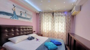 Ein Schlafzimmer mit einem großen Bett, einem Kopfteil, einem Nachttisch, einem Fenster mit Vorhängen und einer Klimaanlage.