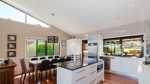 Une cuisine moderne dotée d’un îlot central, de meubles blancs et offrant une vue sur l’extérieur grâce à de grandes fenêtres.