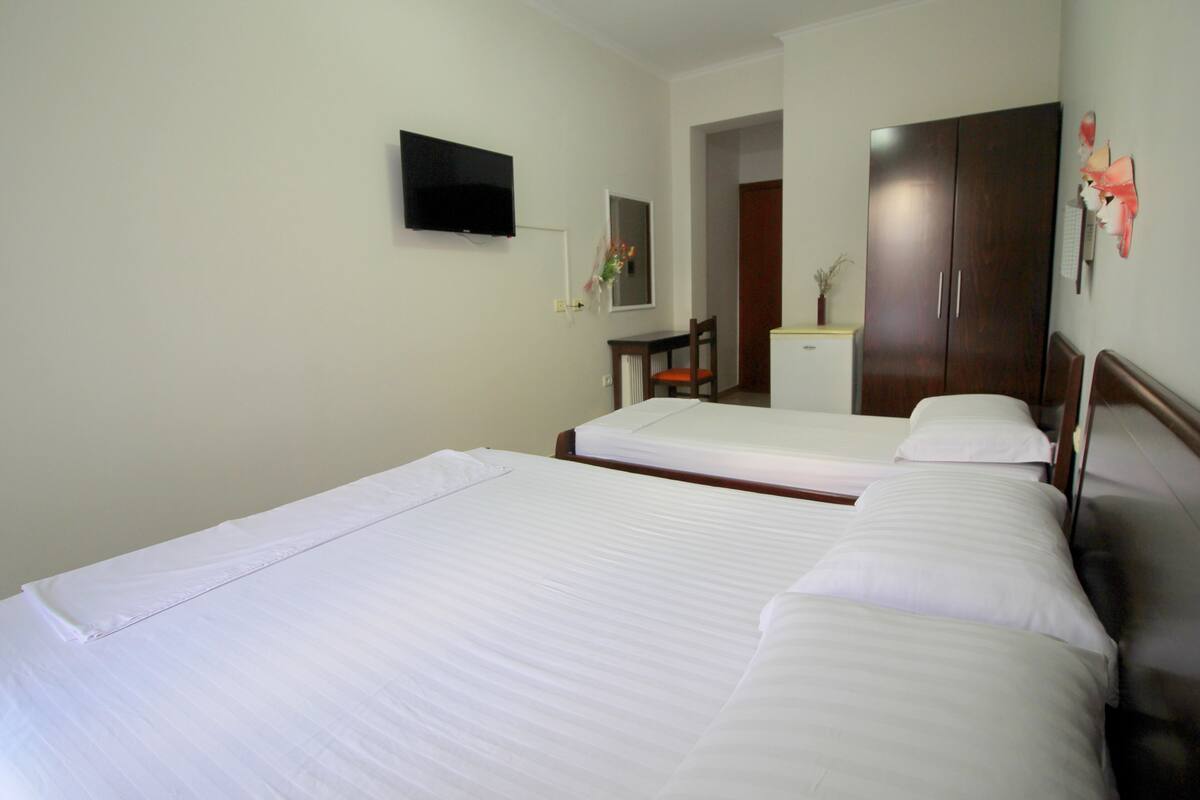 A hotel room with two single beds, a television on the wall, a desk with a chair, and a wardrobe.