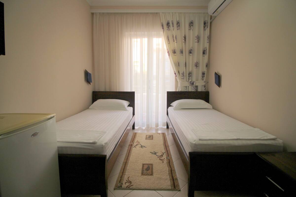 A room with two single beds, a small table, and a refrigerator.