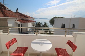 A balcony with two red chairs and a small white table, overlooking a body of water and distant mountains. - Elena Hotel (Sarandë)