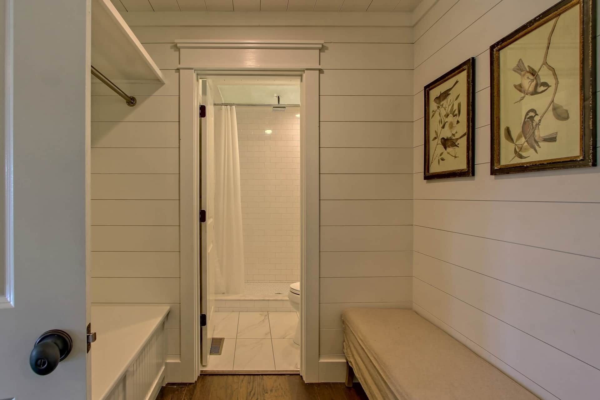 A narrow hallway with a shower area, a bench, and two framed pictures on the wall.