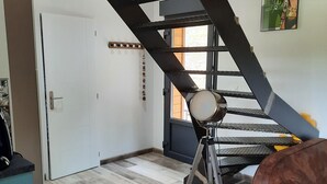 A room with a wooden ceiling, a staircase, a tripod, a chair, and a couch.
