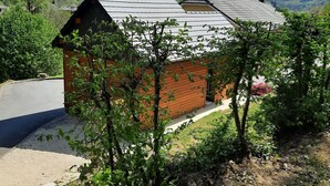 A small brick house with a sloped roof, surrounded by greenery and a clear sky.
