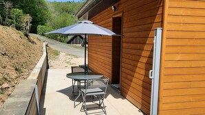 A wooden building with a patio area featuring a table and chairs, a covered umbrella, and a flower bed.