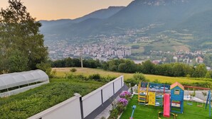 Un jardin sur le toit comprenant un espace de jeux pour enfants, une serre et une vue sur la ville et les montagnes en arrière-plan.