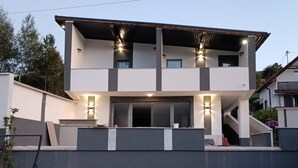 Une maison moderne à deux étages, dotée d’un toit plat, de grandes fenêtres et d’un balcon.