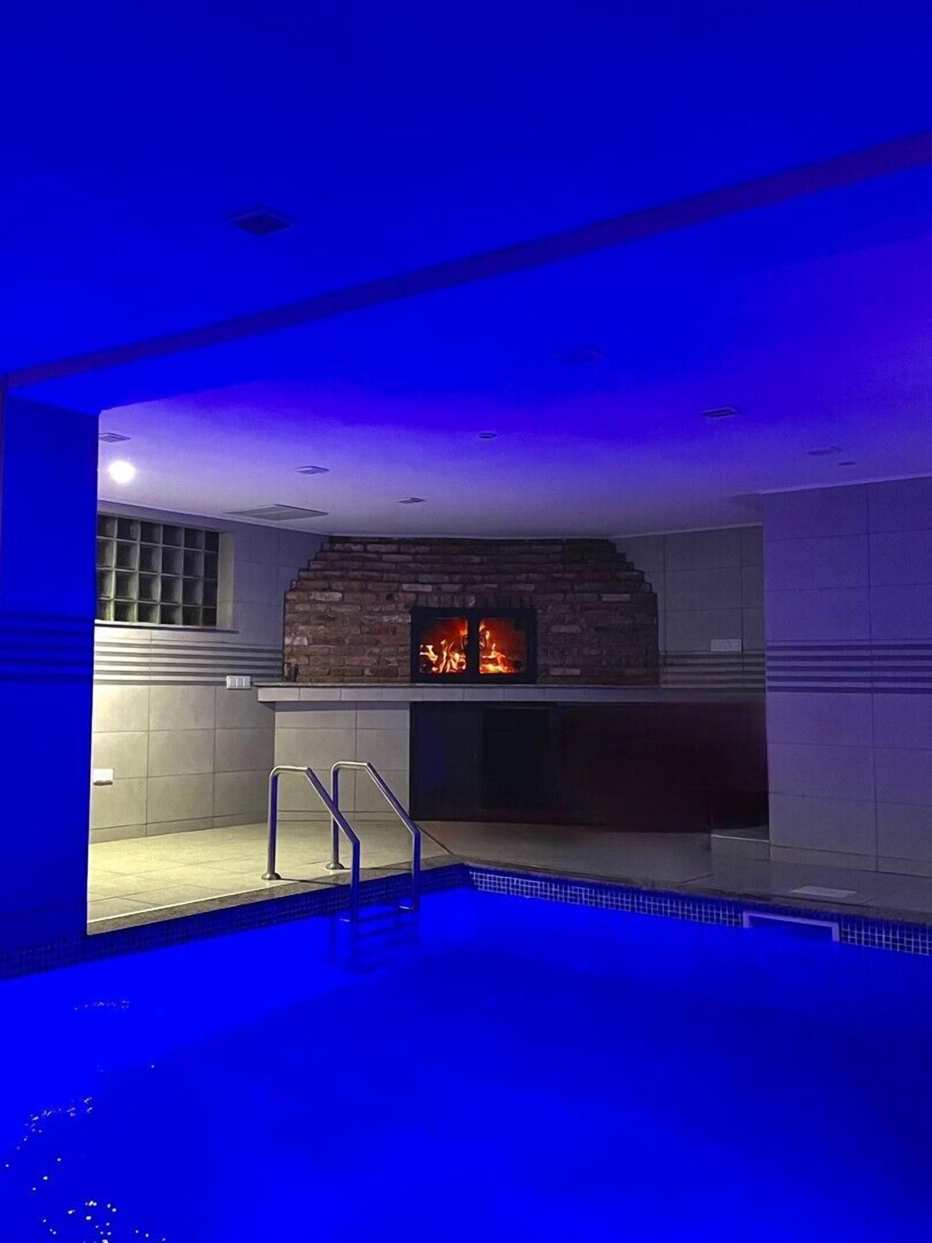 Ein moderner Poolbereich im Innenbereich mit einem Steinkamin und einem Pool mit blauer Beleuchtung.
