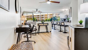 Cocina moderna con armarios blancos, microondas y cafetera. Hay un comedor con mesa y sillas, y un ventilador de techo.