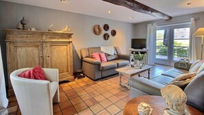 Een woonkamer met een bank, een witte fauteuil, een houten kast en een televisie.