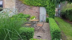 Een tuin met een tafel en stoelen, een grindpad en een muur van baksteen met klimop.