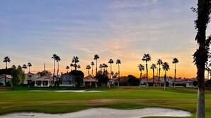 Un campo de golf con búnkeres de arena, palmeras y casas al fondo.