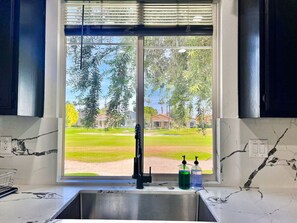 A kitchen with a large window, a stainless steel sink, and a marble countertop.