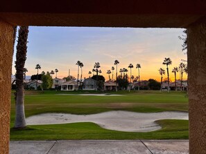 A golf course with sand bunkers, palm trees, and houses in the background.