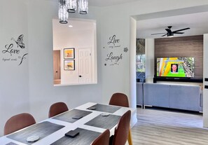 A modern dining area with a table set for four, a television in the background, and decorative wall decals.